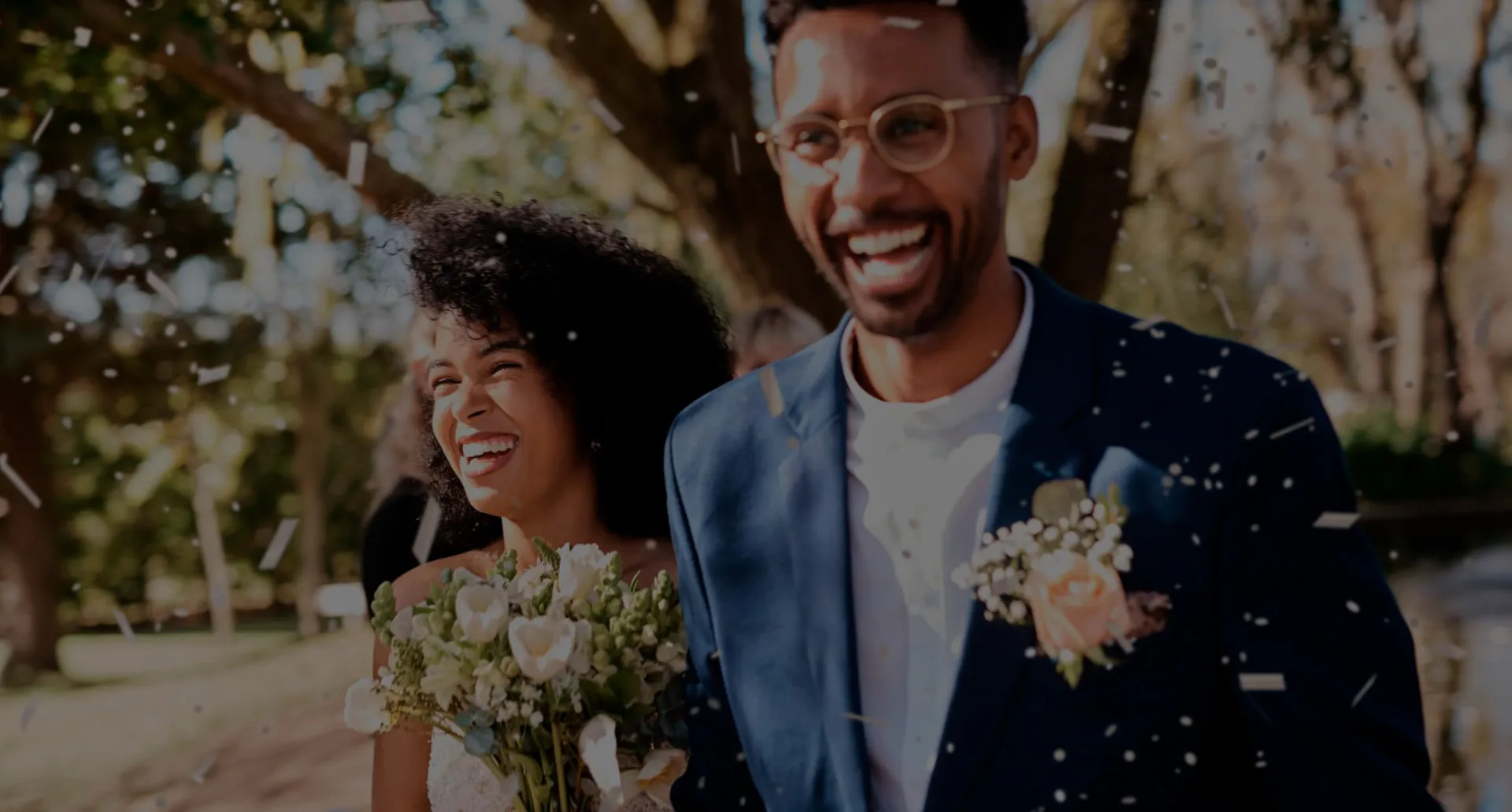 O dia mais especial da sua história começa com uma boa organização. Casal sorridente, vestido de noivos, sendo coberto por pétalas em uma celebração ao ar livre.